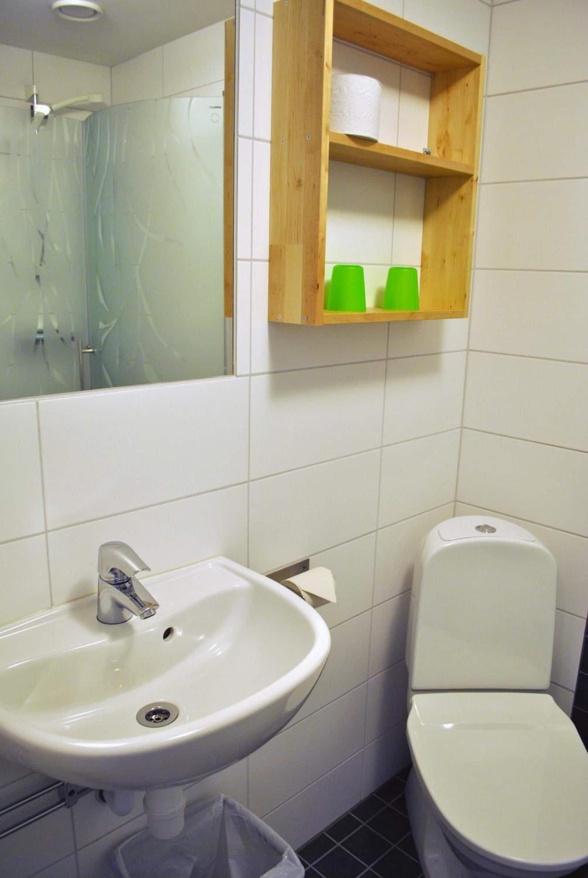 Une salle de bain avec un lavabo blanc, des toilettes et une étagère en bois au-dessus des toilettes.