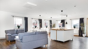 A spacious living area with a grey sofa, a white kitchen island, and large windows with curtains. - Brink Hotell (Eslöv)