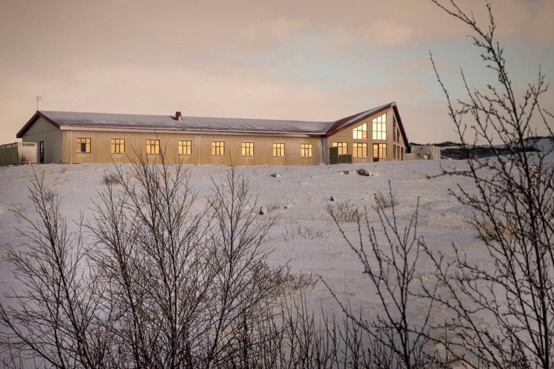 A long, single-story building with large windows and a sloped roof, surrounded by snow.