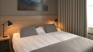 A neatly made bed with a headboard, two bedside lamps, and a painting on the wall. - Hotel Gullfoss (Bláskógabyggd)
