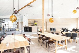 Un comedor amplio con varias mesas y sillas, una cocina al fondo y lámparas esféricas colgantes.