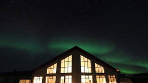 Un edificio con grandes ventanales y un techo triangular, bajo un cielo estrellado con auroras boreales visibles.