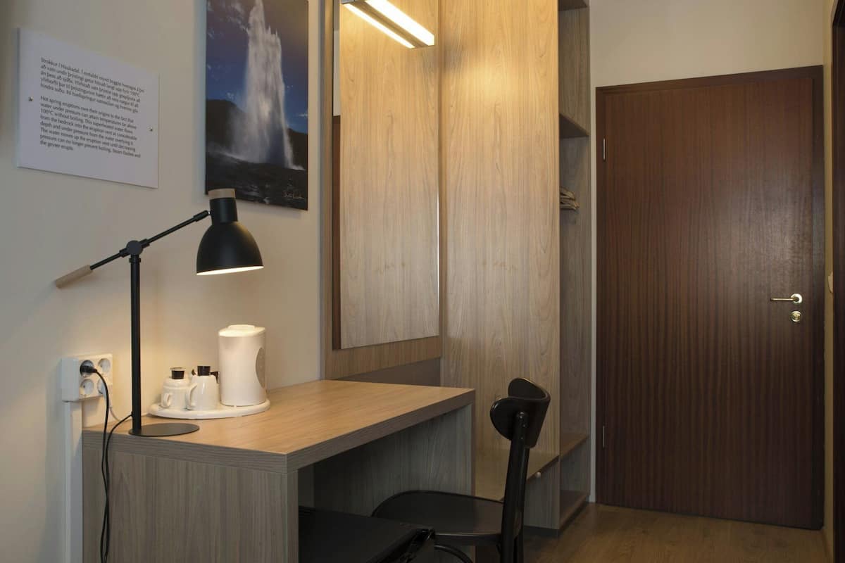 Una habitación pequeña y moderna con un escritorio, una silla, una lámpara y una puerta.