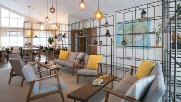 A spacious lounge area with modern furniture, pendant lighting, and a large window providing natural light. - Hotel Gullfoss (Bláskógabyggd)