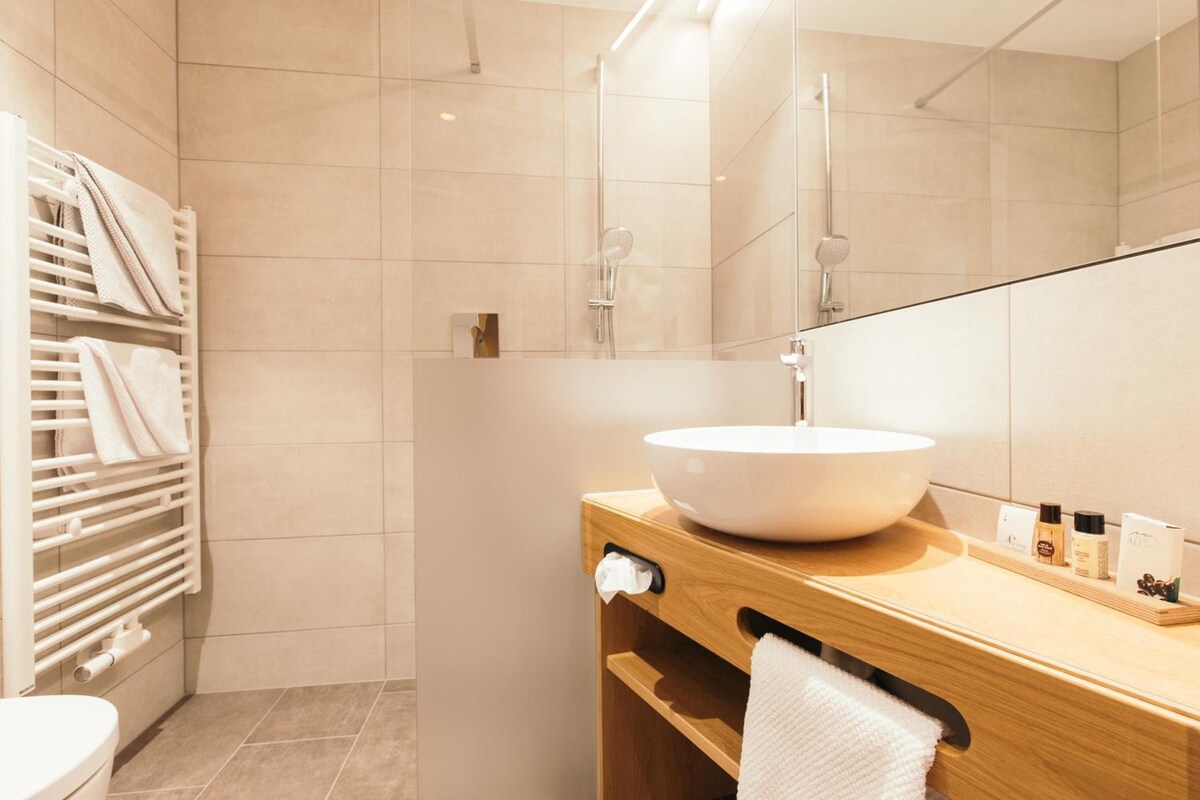 A modern bathroom with a large mirror, a white sink, and a towel rack.