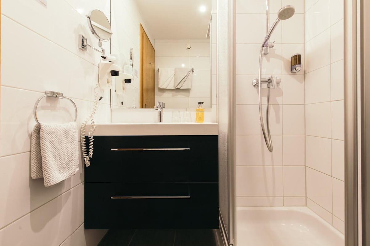 Een badkamer met een douche, een spiegel, een handdoekhouder en een wastafel.