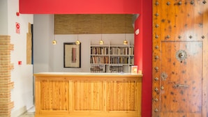 Un mostrador de recepción de madera con estantería, luces colgantes y pared roja.