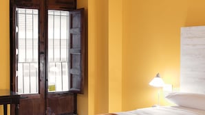 Una habitación con cama, mesita de noche, lámpara y ventana con persianas de madera.