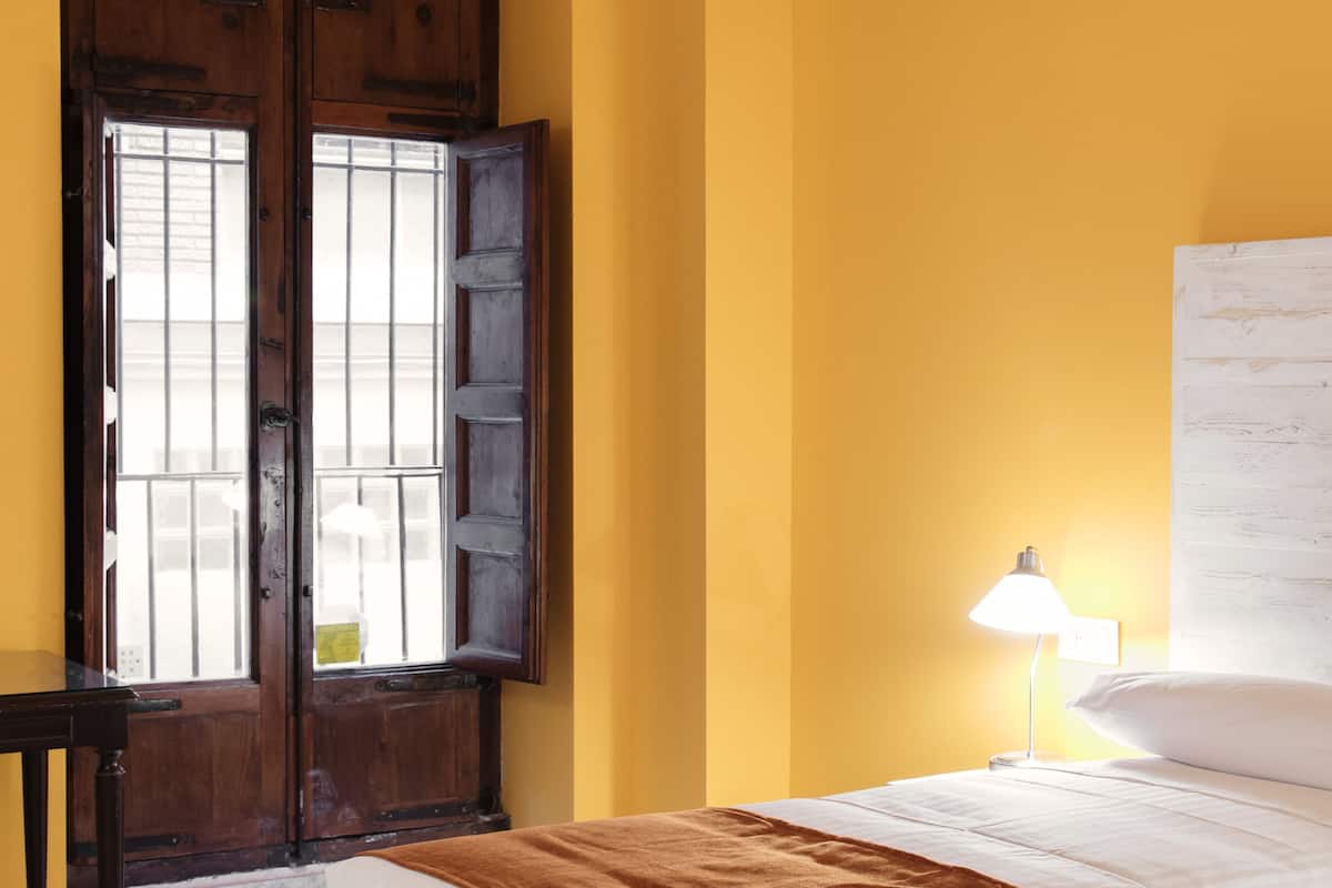 A room with a bed, a nightstand, a lamp, and a window with wooden shutters.