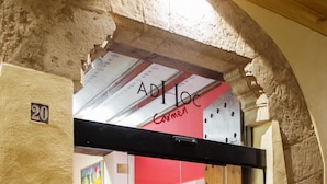 Entrada de un hotel con puerta de vidrio, un letrero rojo en la parte superior y una recepción en el interior.