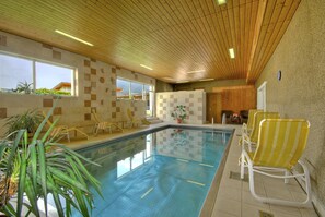 Una piscina techada, sombrillas, sillones reclinables de piscina