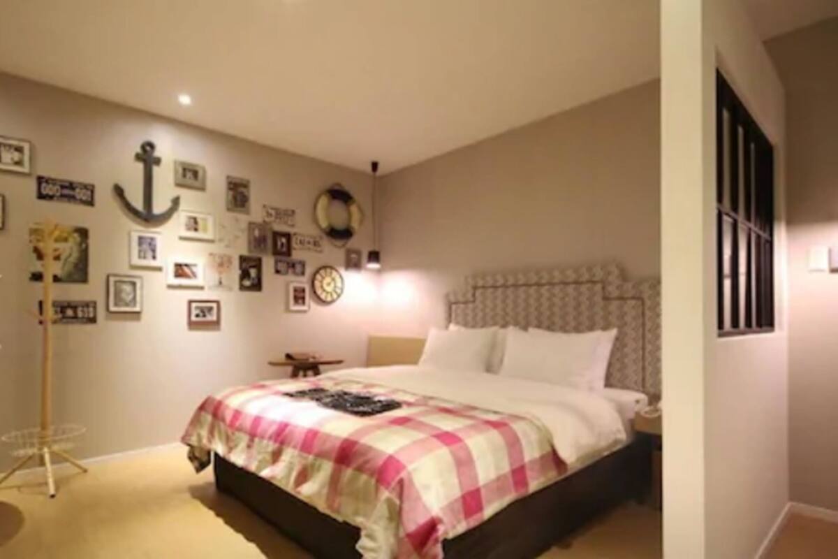 Un dormitorio con cama, escritorio y silla. Hay adornos en la pared y una ventana.