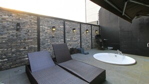 A rooftop patio with a stone wall, a lounge chair, a sun lounger, and a freestanding bathtub. - 25 Hours Hotel (Busan)