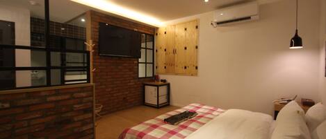 A bedroom with a checkered bedspread, a television mounted on a brick wall, and a wooden wardrobe.