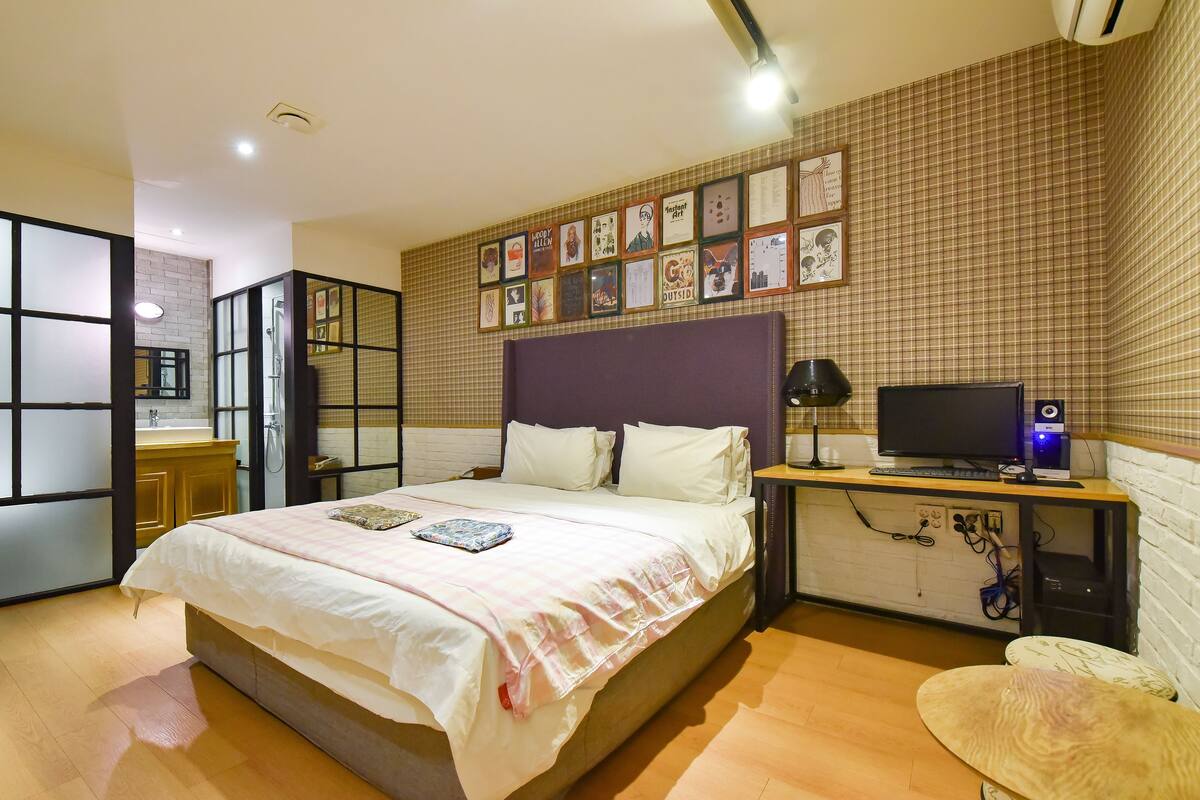 Un dormitorio con una cama, un escritorio con computadora, un televisor y una pared con cuadros enmarcados.