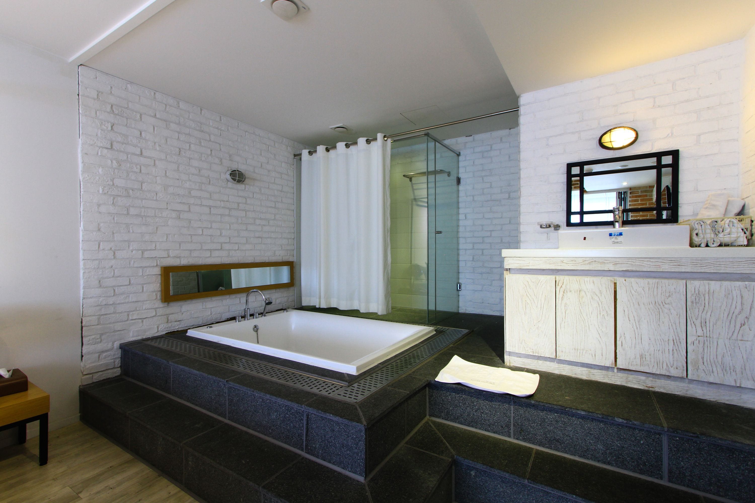 Un baño moderno con una bañera grande, un box de ducha de vidrio y una pared de ladrillo blanco.