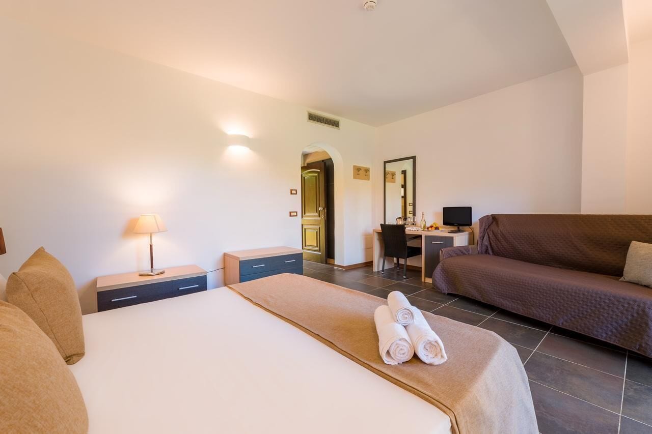 A hotel room with a bed, a desk, a sofa, and a chair.