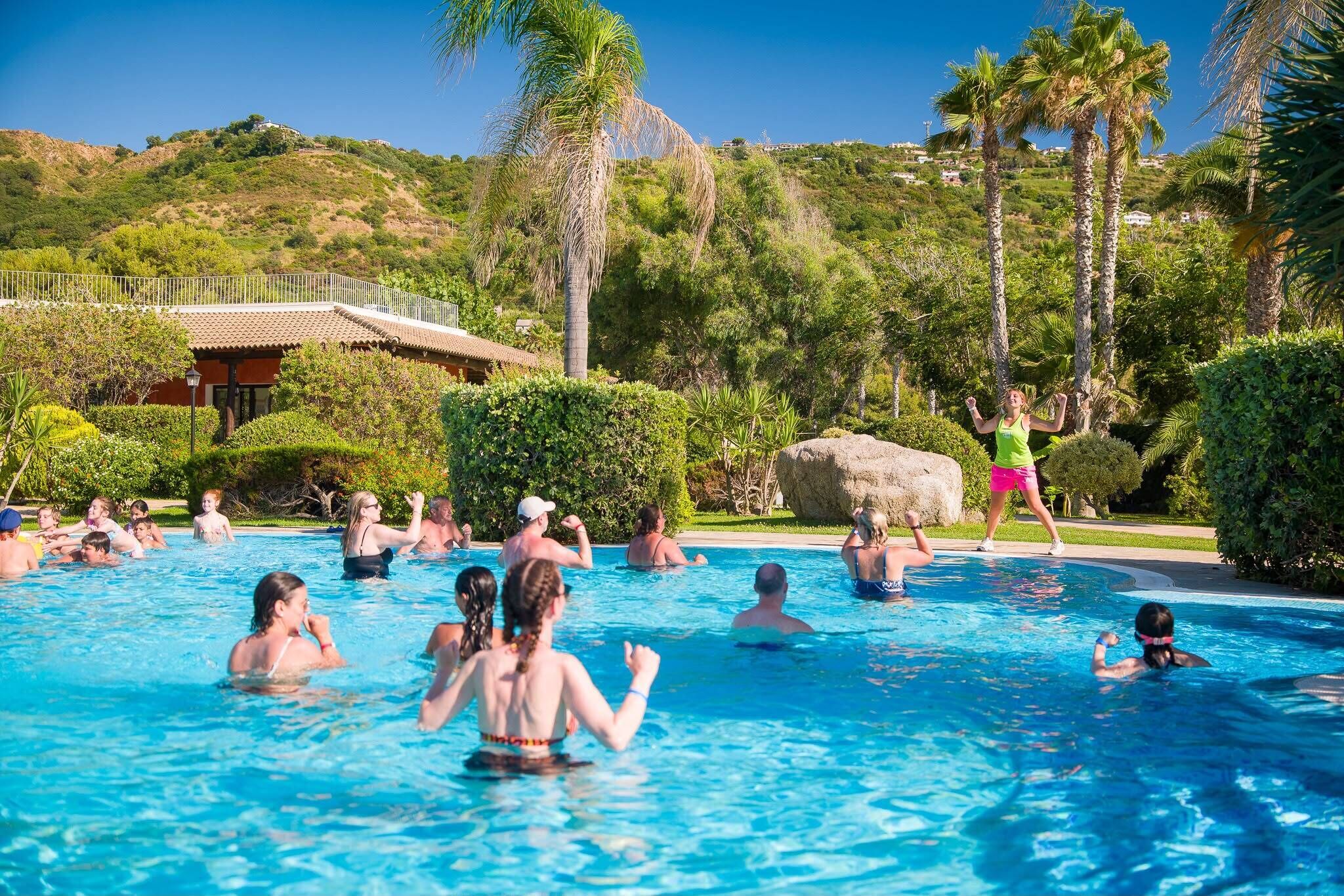 Ein Schwimmbecken mit Personen, umgeben von Grün und einer Hügelkulisse.