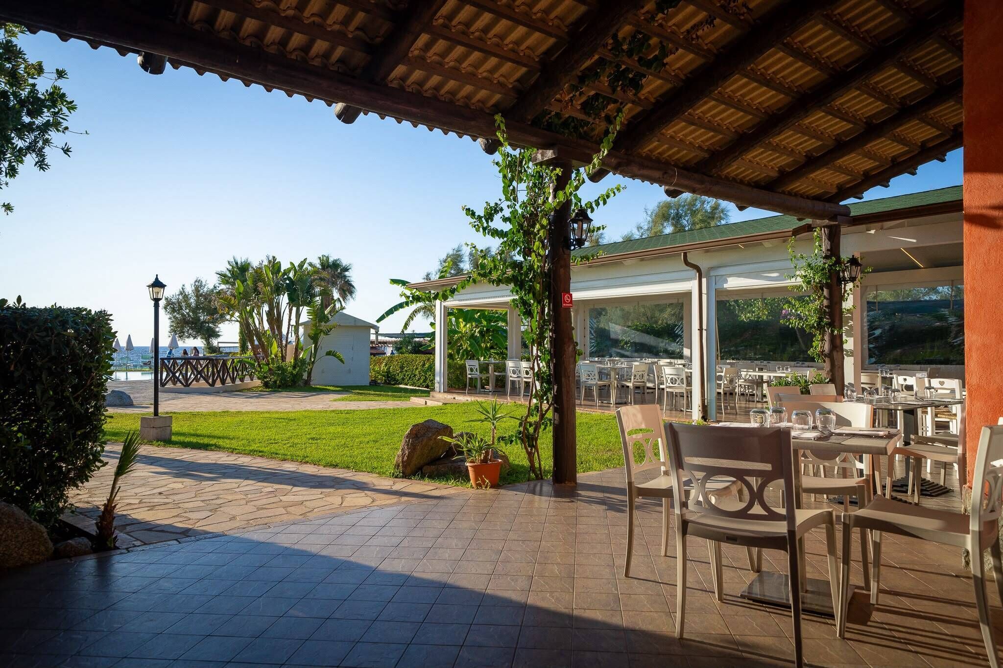 Un patio al aire libre con mesas y sillas, una pérgola y vista al mar.