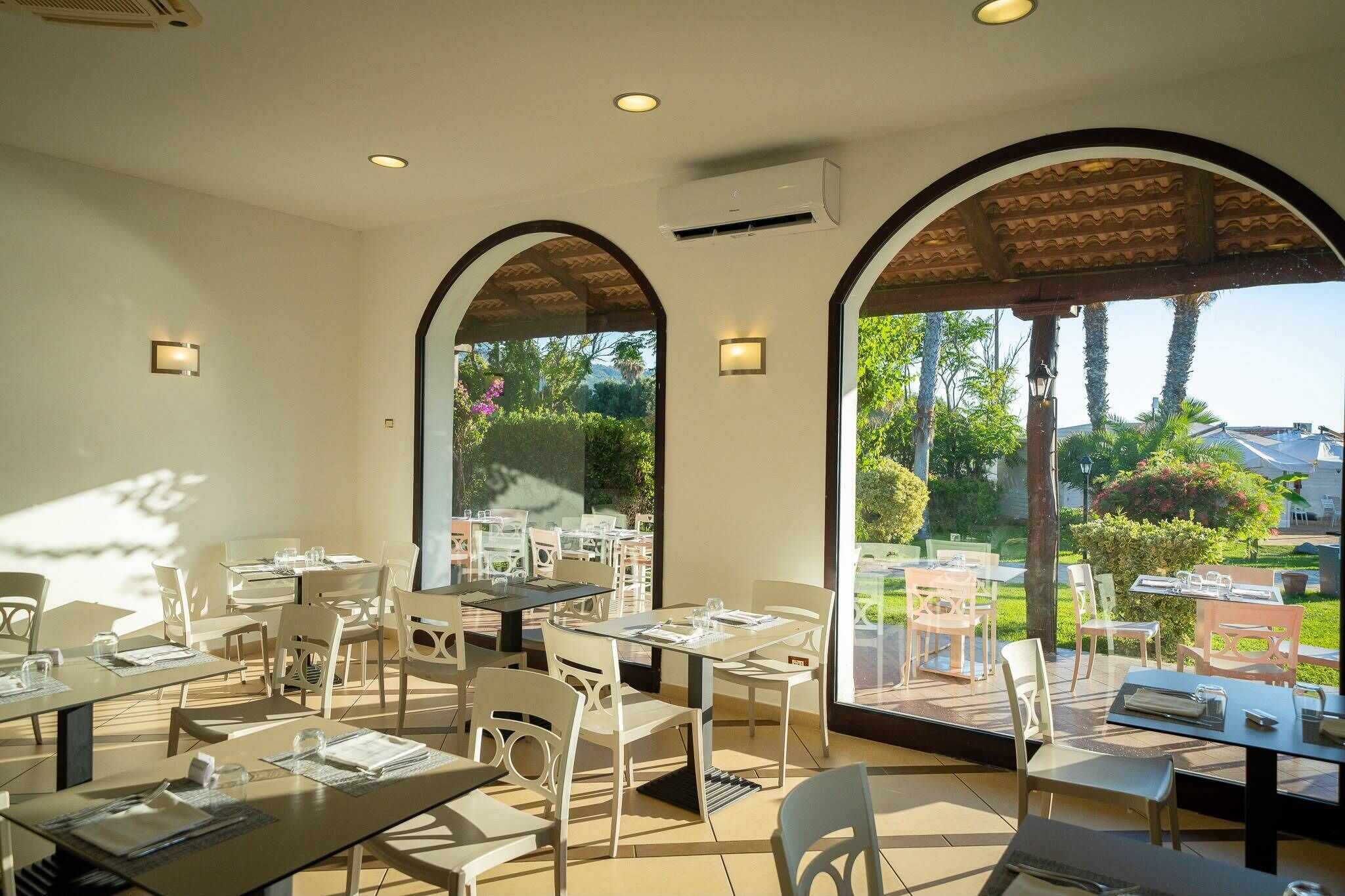 Un'area pranzo all'aperto con tavoli e sedie, ampie finestre e un condizionatore d'aria.