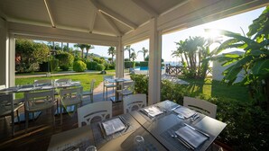 An outdoor dining area with tables and chairs, a pool, and lush greenery in the background. - Borgo del Principe by Valentour (Zambrone)