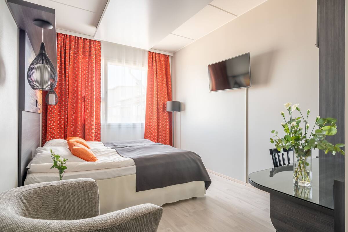 Une chambre d’hôtel moderne équipée d’un lit, d’une chaise, d’une télévision et d’un vase avec des fleurs.
