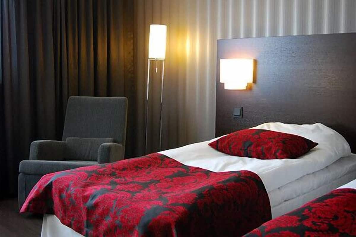 Une chambre d’hôtel avec un lit, une chaise, une table de chevet et une lampe fixée au mur.