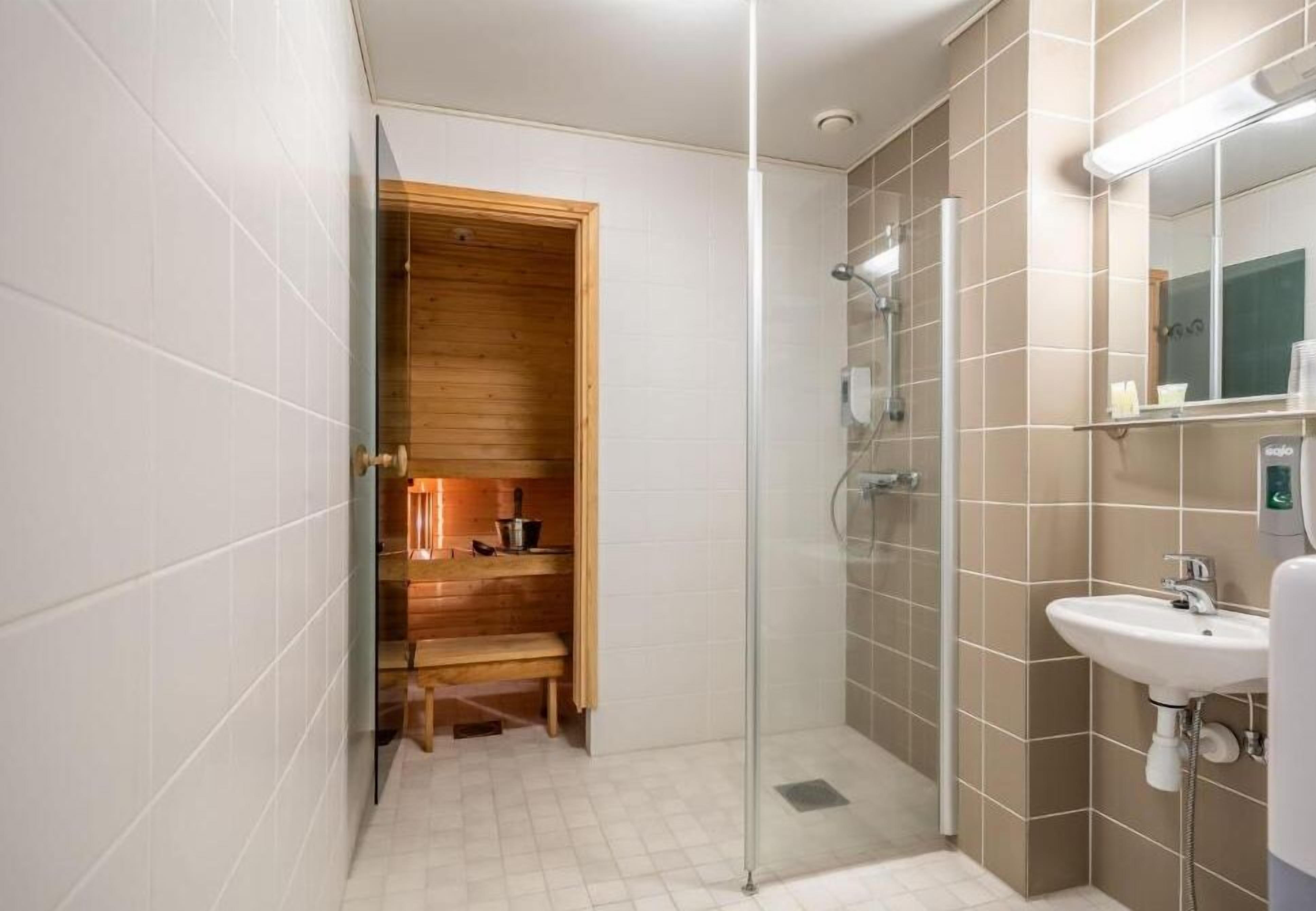Une salle de bain moderne avec une douche à parois de verre, un sauna en bois et un lavabo blanc.