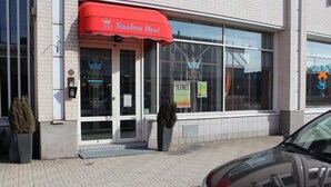 The exterior of a hotel with a red awning, a glass entrance, and a car parked in front. - Hotel Raahen Hovi (Raahe)