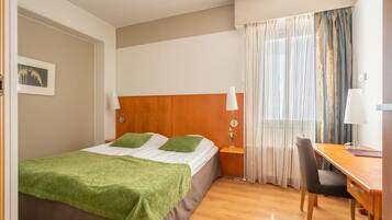 A hotel room with a bed, a desk, a chair, a nightstand, and a window with curtains.