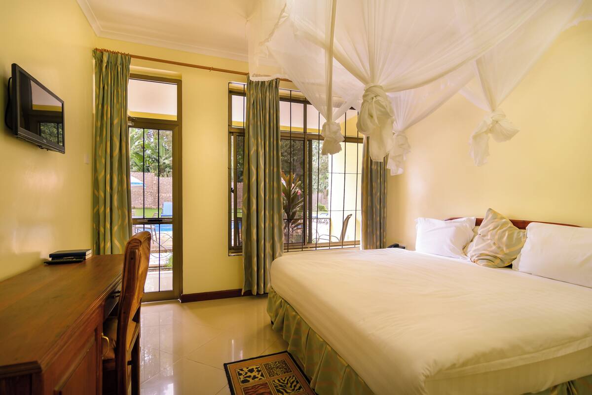 Habitación de hotel con cama, escritorio, silla, televisor y ventana con cortinas.