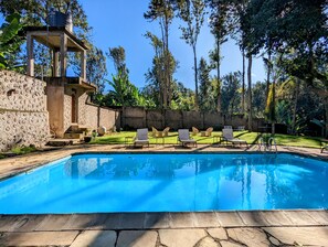 A swimming pool with lounge chairs and a stone wall. - Mvuli Hotel (Arusha)