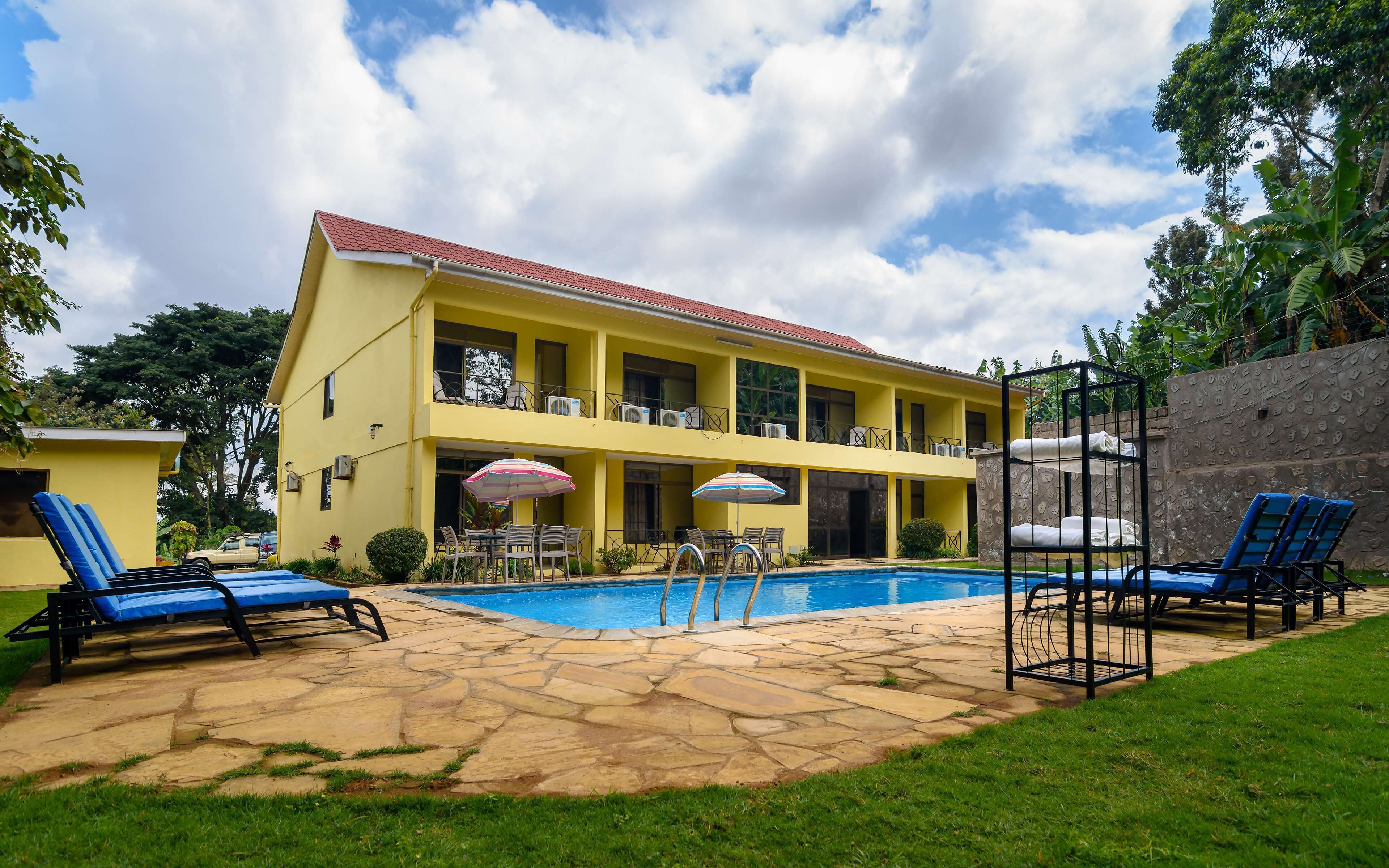 A two-story yellow building with a swimming pool, outdoor seating, and a stone patio.
