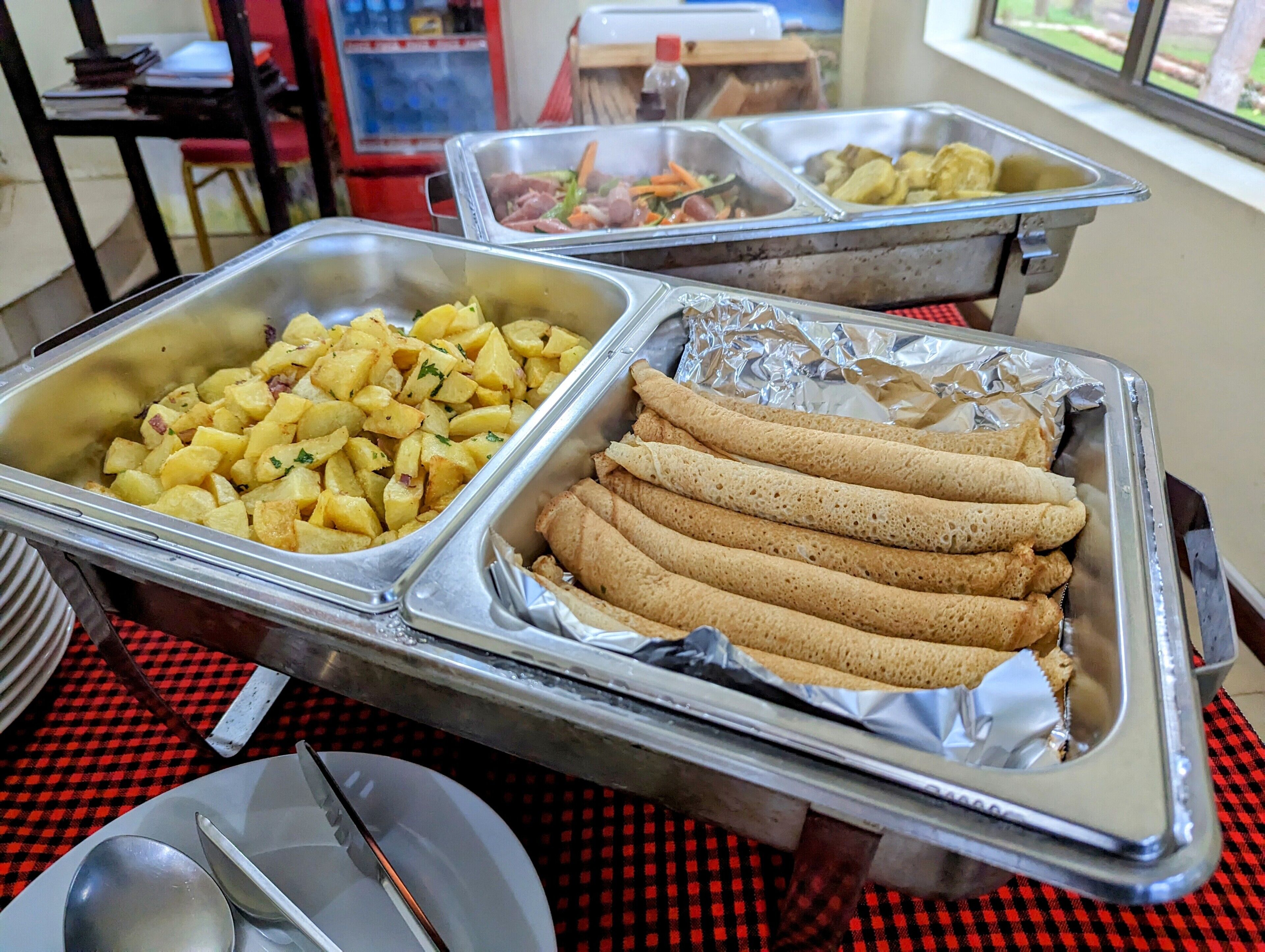 A buffet with trays of food including potatoes, rolls, and other dishes.