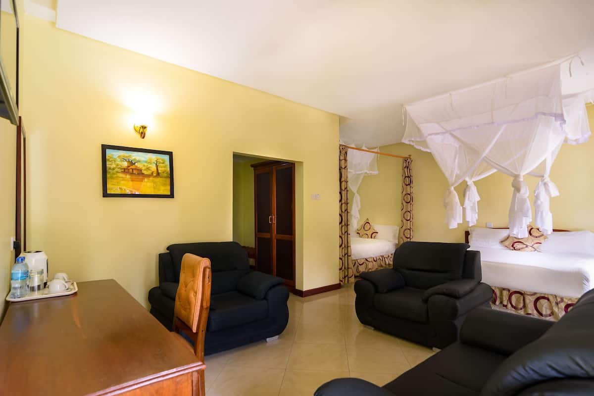 Habitación de hotel con una cama, dos sillones, una mesa de madera con una bandeja de objetos, un cuadro en la pared y una mosquitera sobre la cama.