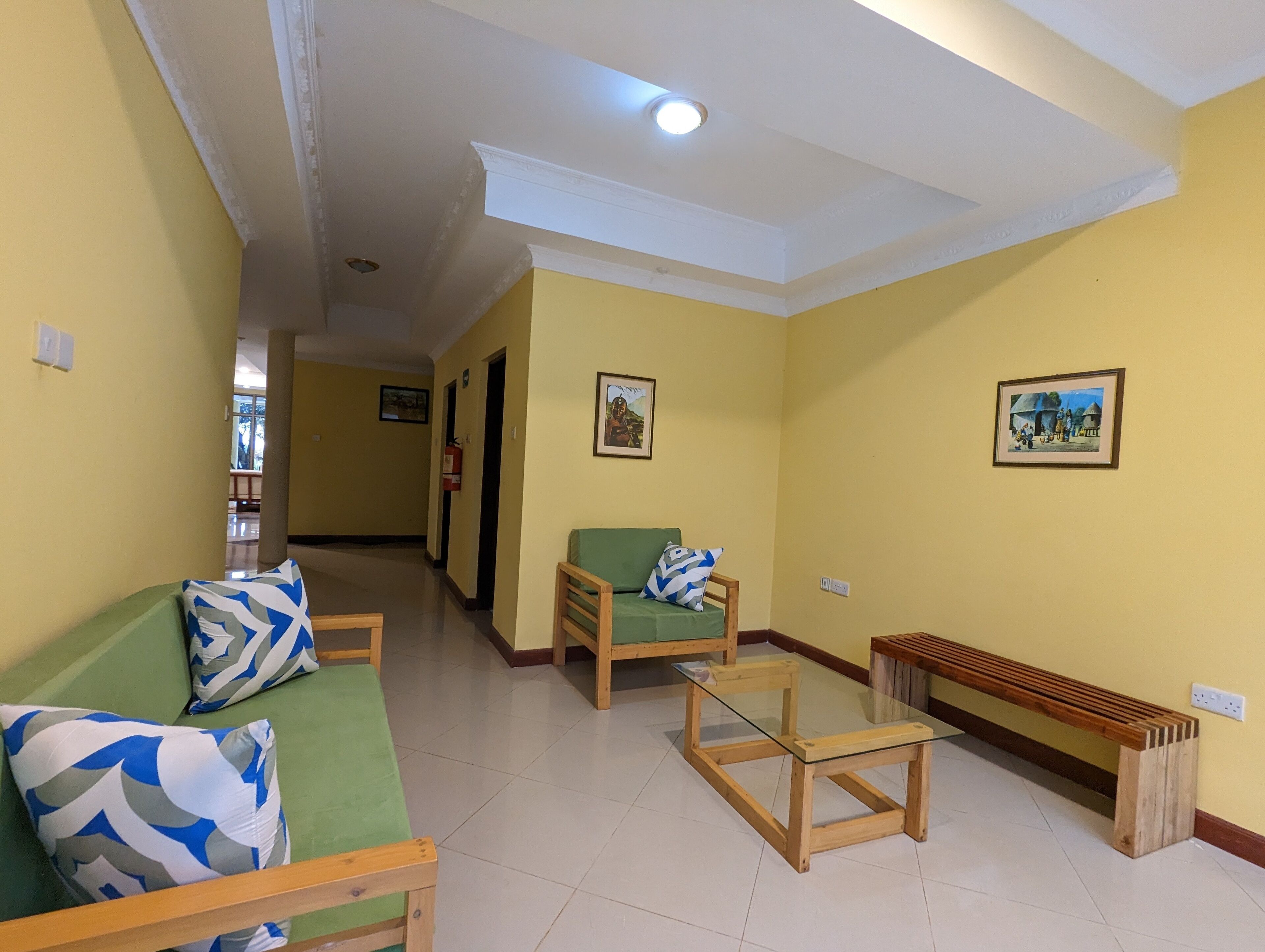 A hallway with a green sofa, a wooden bench, and a glass table. There are two framed pictures on the walls.