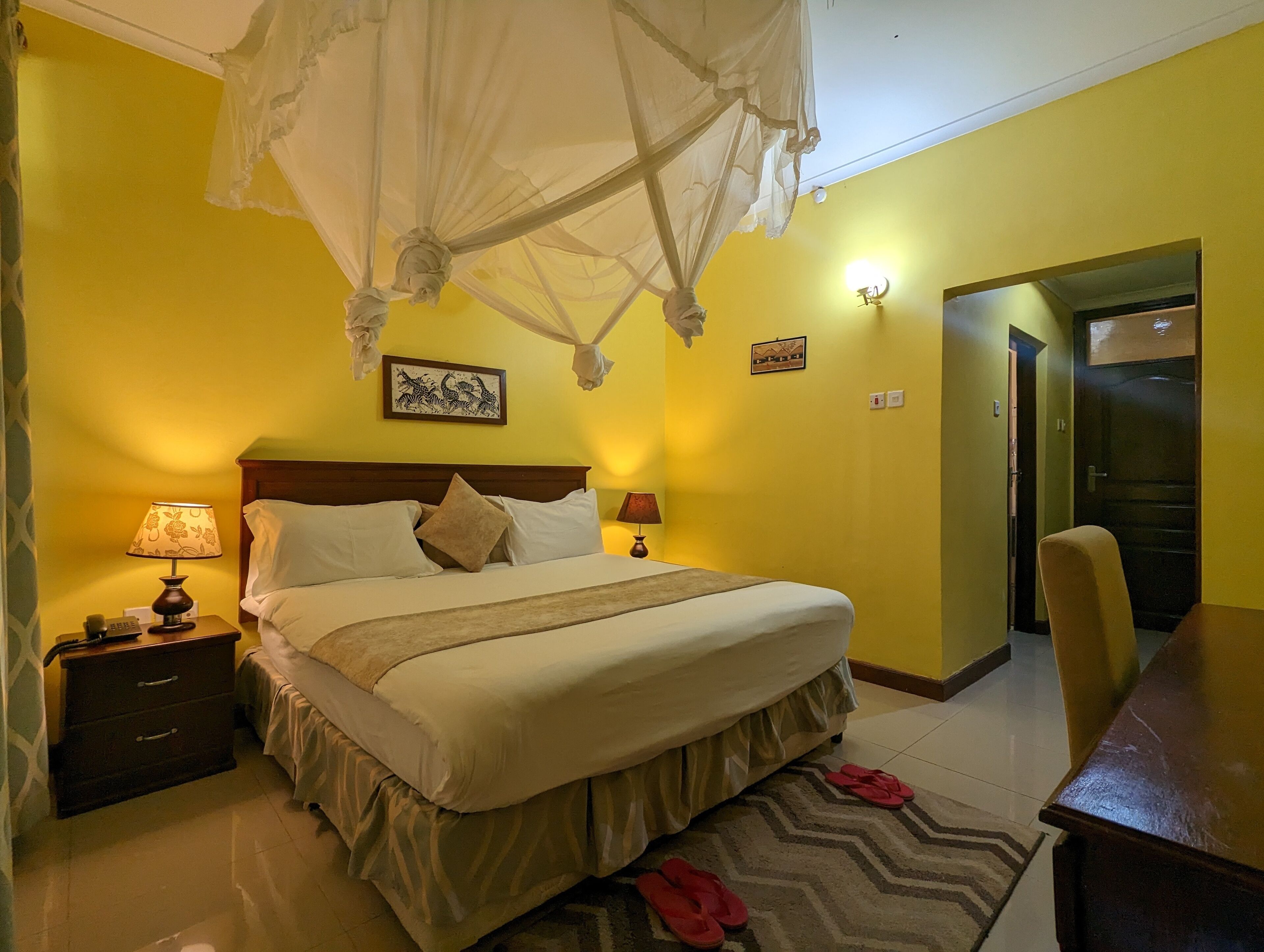 Una habitación de hotel con cama, lámparas de noche, mesita de noche, una silla y una puerta.