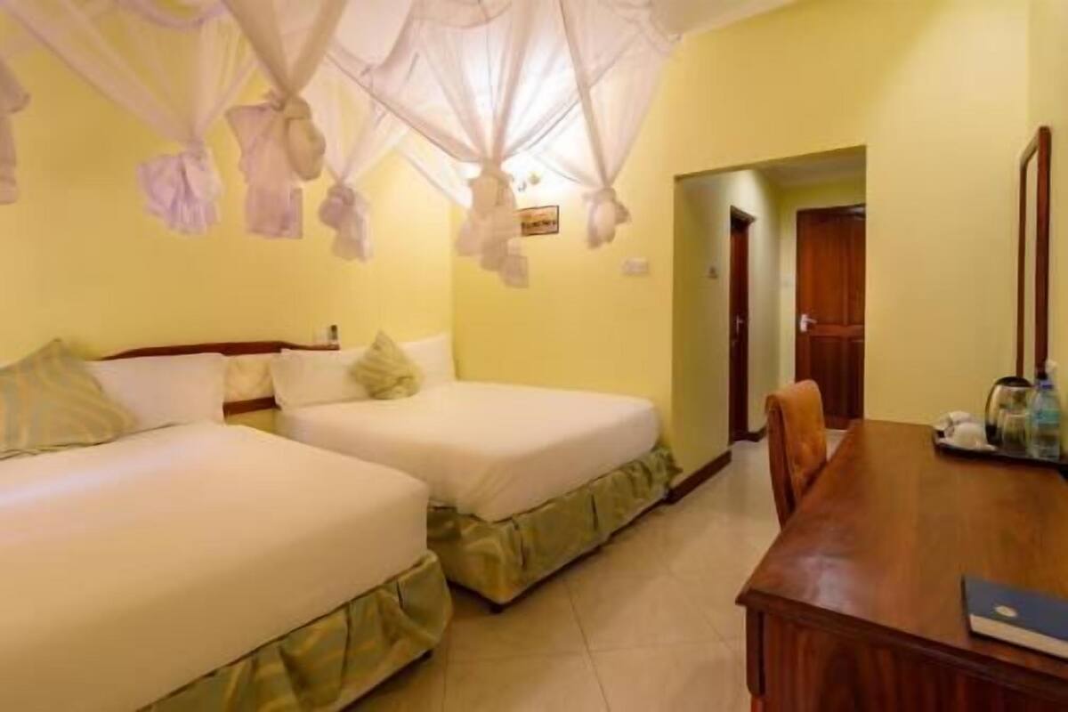 Una habitación de hotel con dos camas, una mesa de madera y una puerta que da a otra habitación.