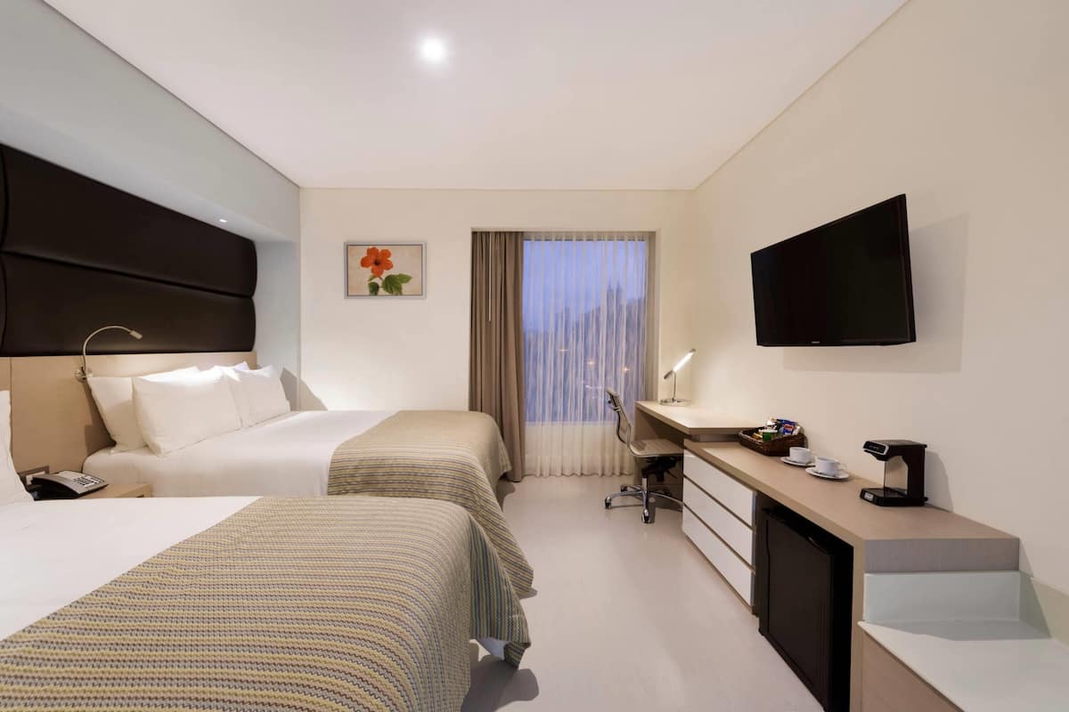 Habitació d'hotel amb dos llits, una taula de treball, televisió i finestra amb cortines.