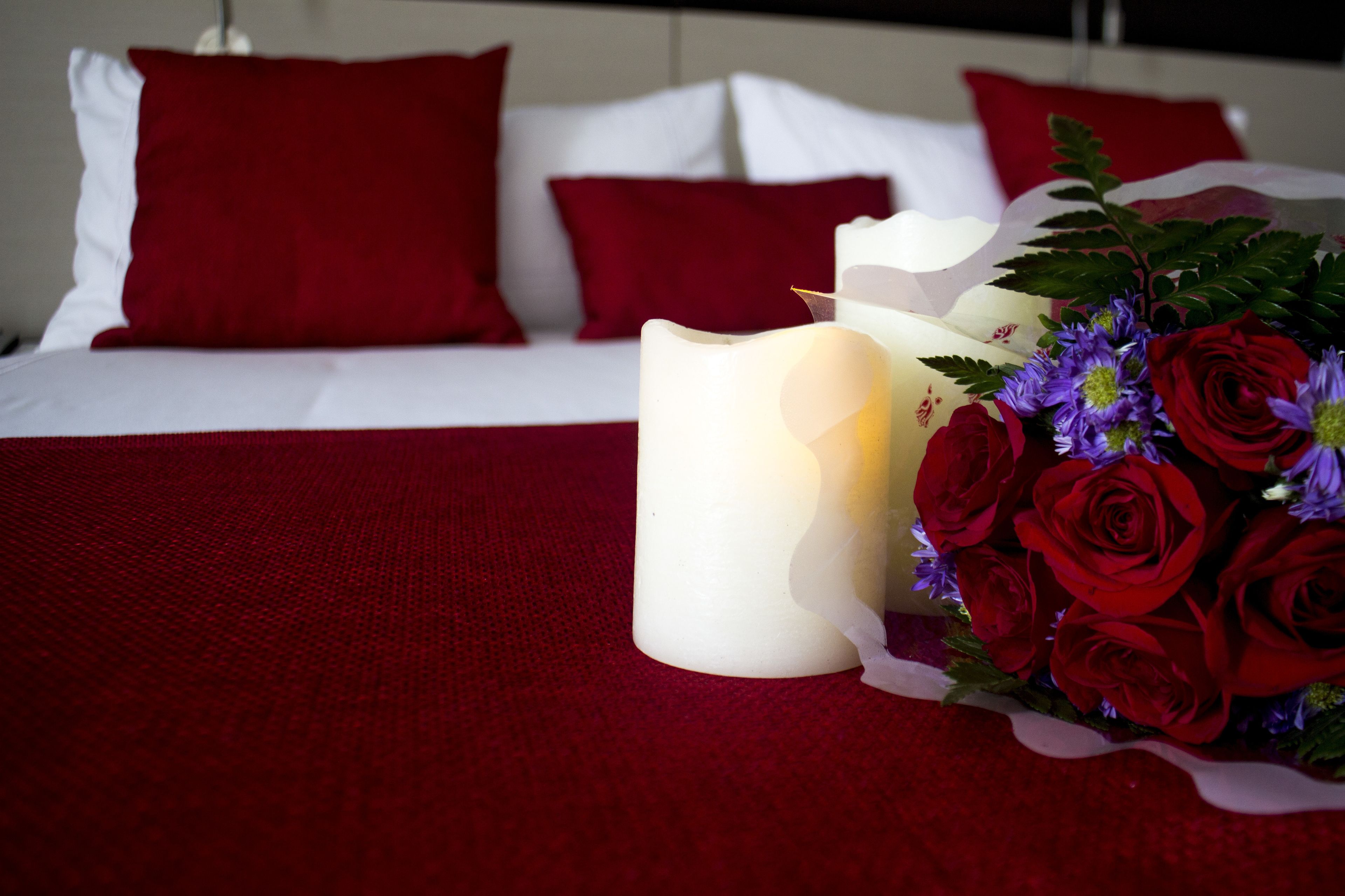 A bed with red and white bedding, a white candle, and a bouquet of red roses.