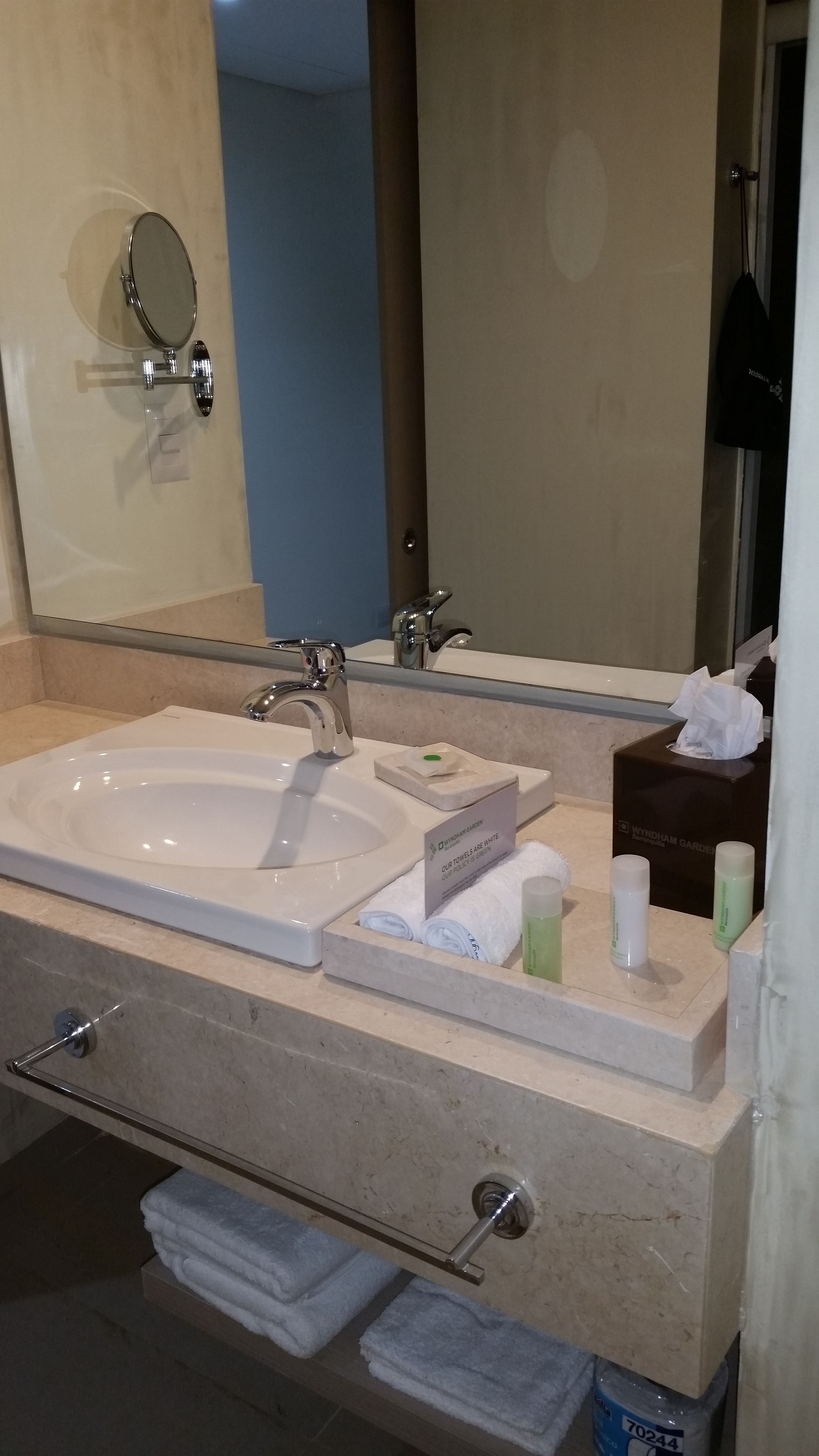 Un baño con lavamanos blanco, un espejo, dispensador de toallas y un tendedero para toallas.