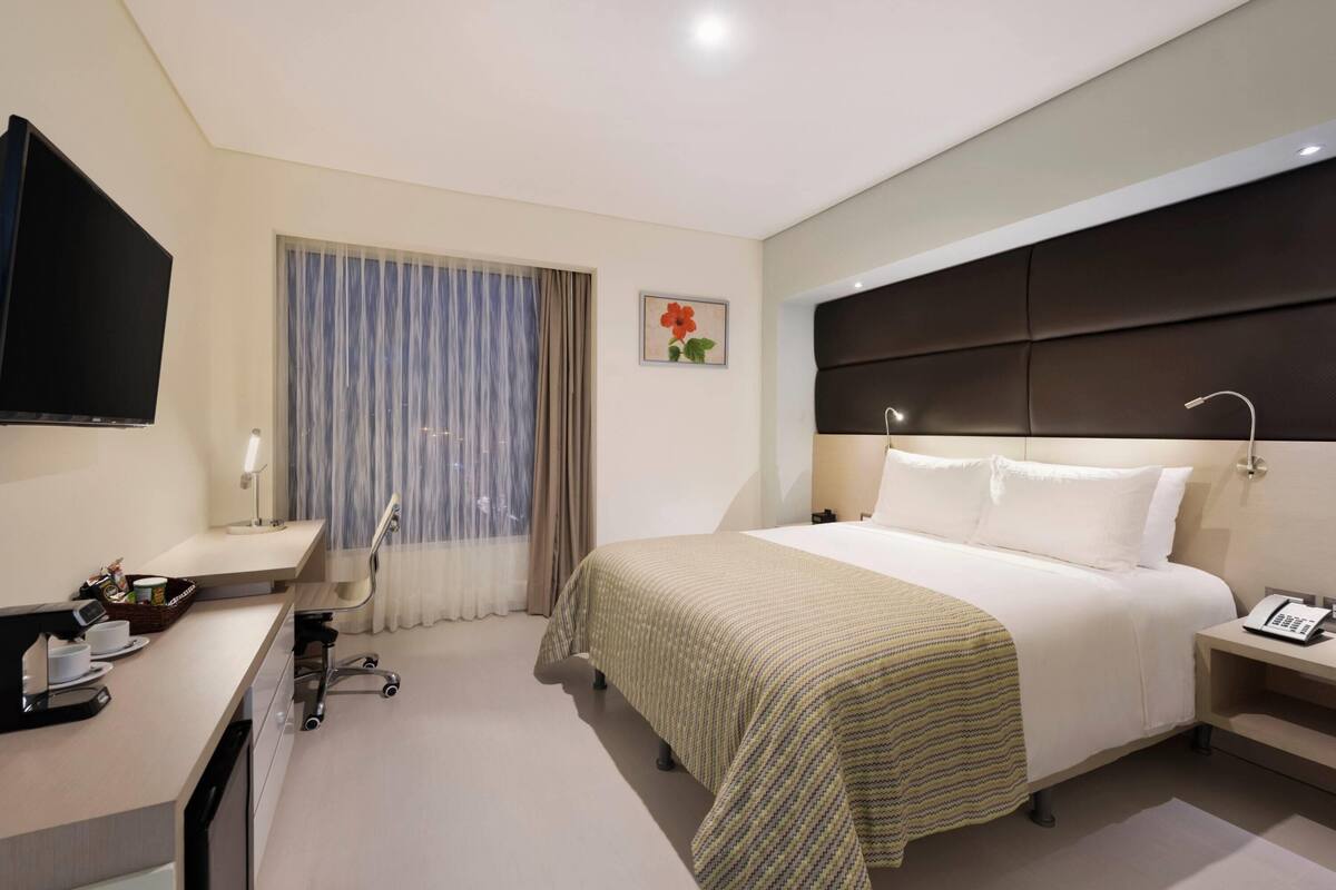 Habitació d'hotel amb un llit, una taula de nit, escriptori amb un ordinador i un televisor.