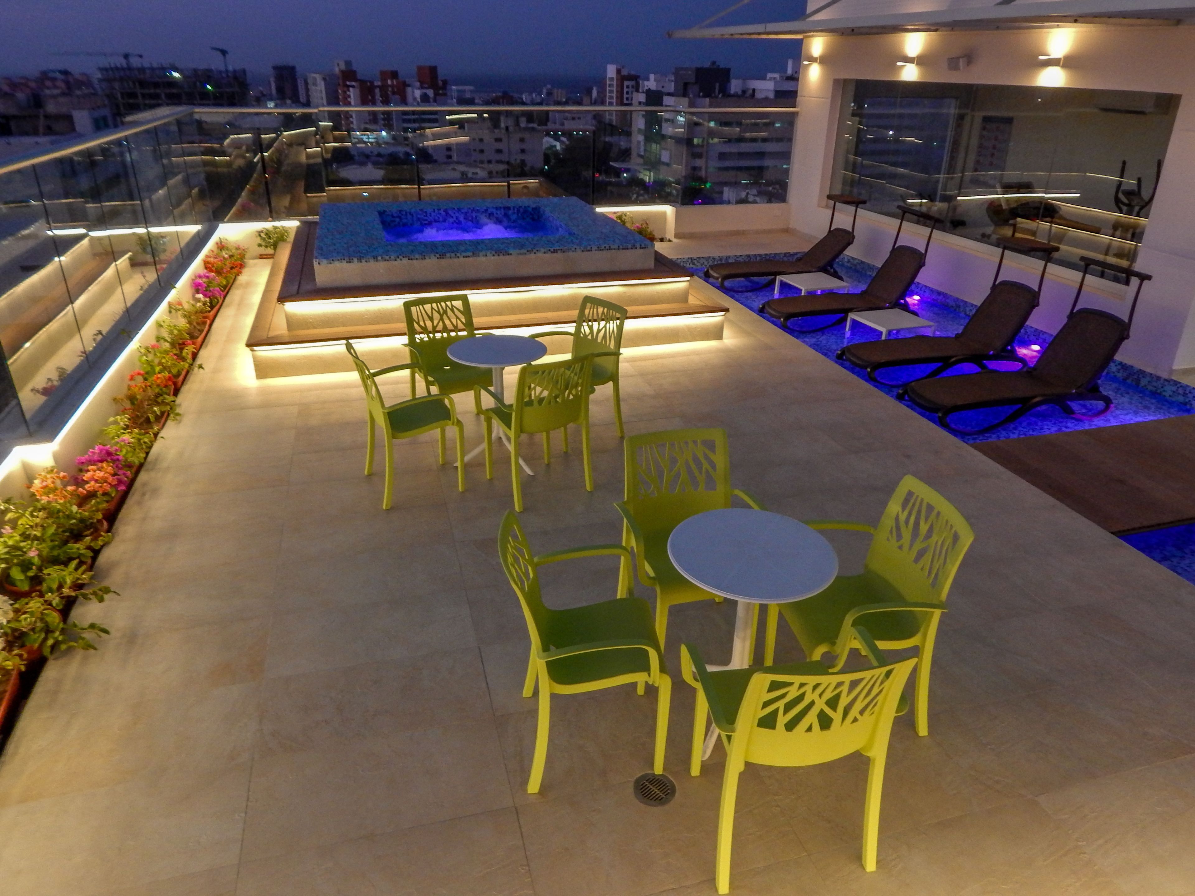 A rooftop terrace with a pool, green chairs, and lounge chairs.