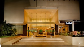Een moderne hotelentree met een receptiebalie, een trap naar de lobby en een restaurant genaamd "Punto Magico" zichtbaar door de glazen deuren.
