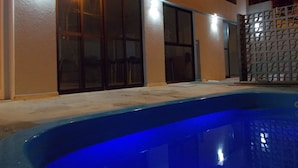 A swimming pool with a blue interior, adjacent to a building with large glass doors and windows, and a metal fence. - Hotel Refugio (Maceió)