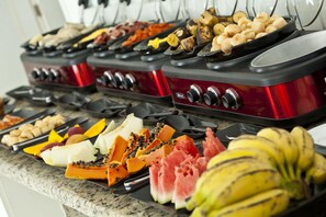 Un bufé con diversas frutas y verduras, incluyendo sandía, papaya y plátanos, dispuesto sobre una encimera de granito.