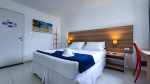 A hotel room with a bed, a desk, and a chair. There is a painting on the wall and a sign on the door. - Hotel Refugio (Maceió)