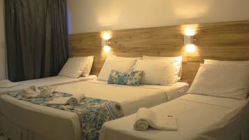 Habitación de hotel con dos camas, cada una con ropa blanca y una manta estampada. Hay dos luces fijadas a la pared sobre las camas y una cortina en el lado izquierdo.