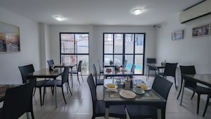 A dining area with tables and chairs, large windows, and an air conditioning unit. - Hotel Refugio (Maceió)