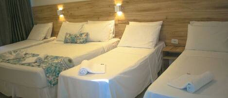 Habitación de hotel con tres camas individuales, cada una con colcha y almohadas blancas, y cabeceros de madera.